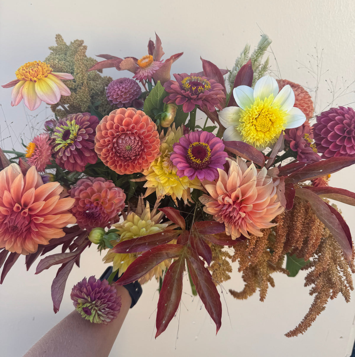 Bouquet of colorful flowers held by a hand against a light background